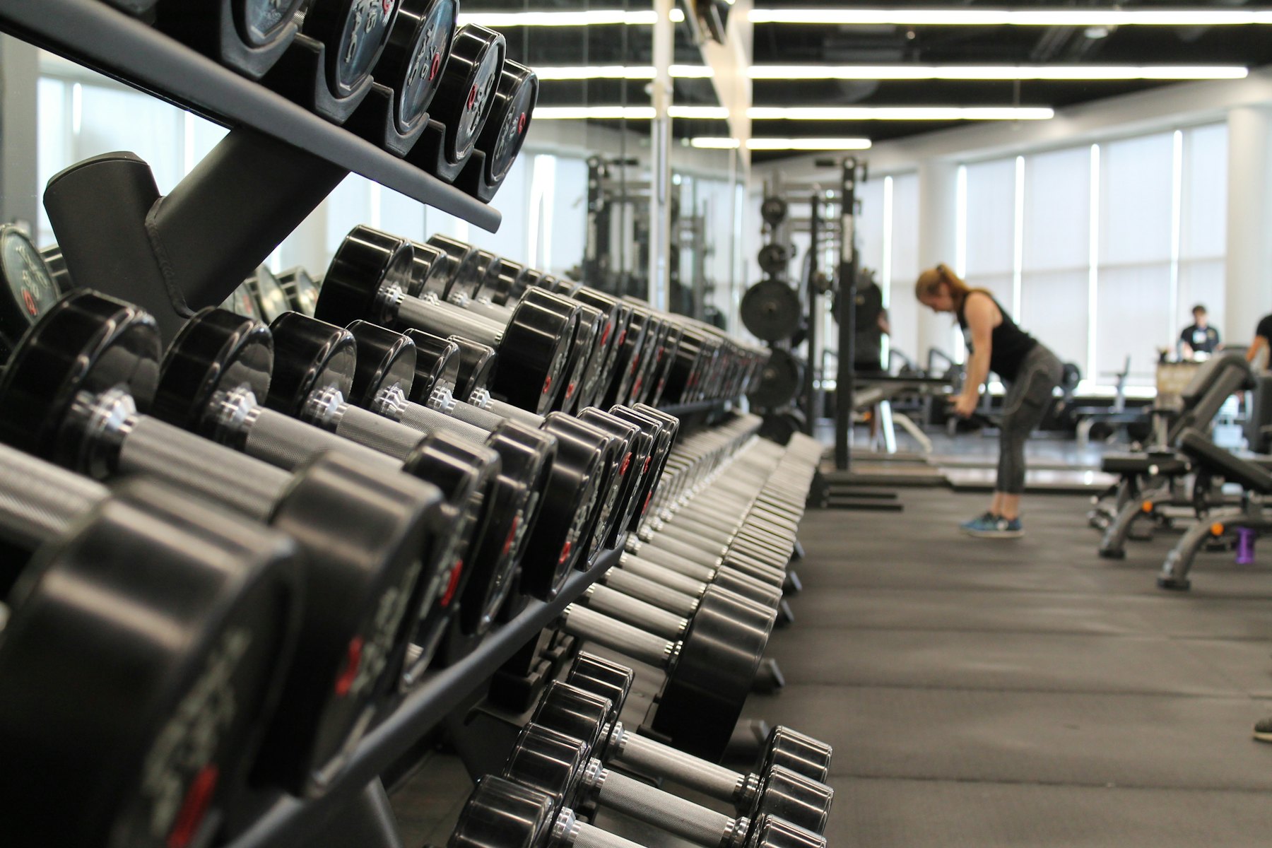 Rows of dumbbells on a rack, with a person training in the background