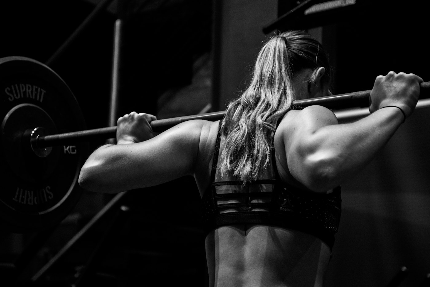 A person holding a barbell across the upper back in a gym